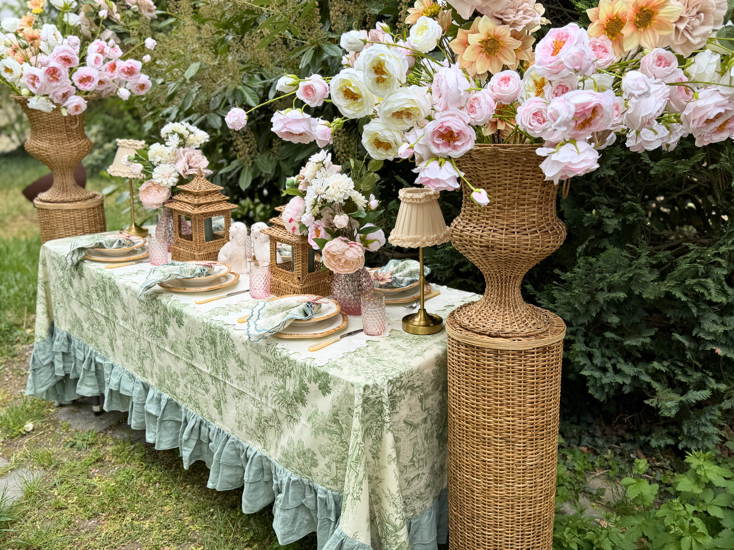 Gedeckter Tisch mit grüner Toile-de-Jouy-Tischdecke und rosa Rosen-Arrangements.