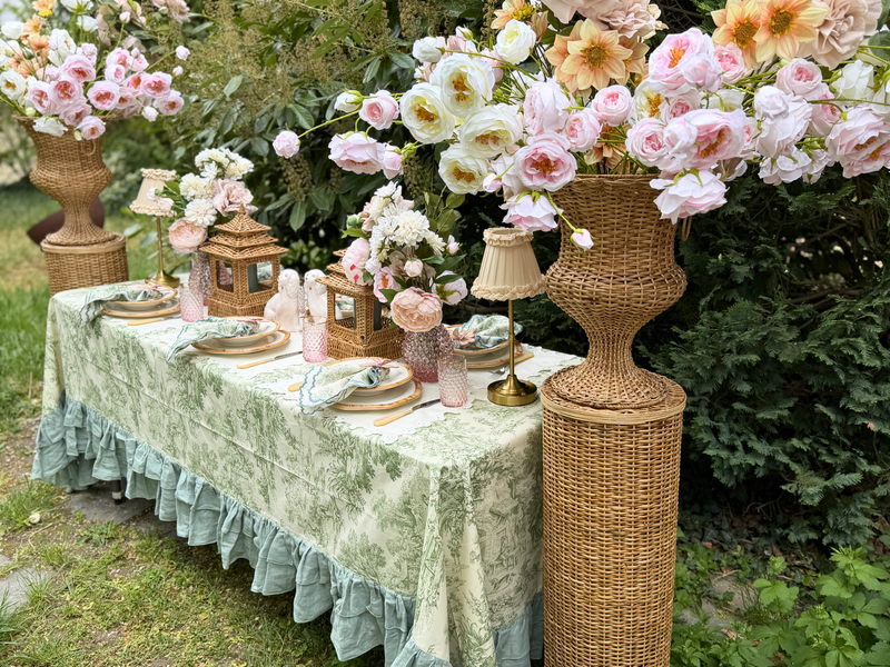 Gedeckter Tisch mit grüner Toile-de-Jouy-Tischdecke und rosa Rosen-Arrangements.