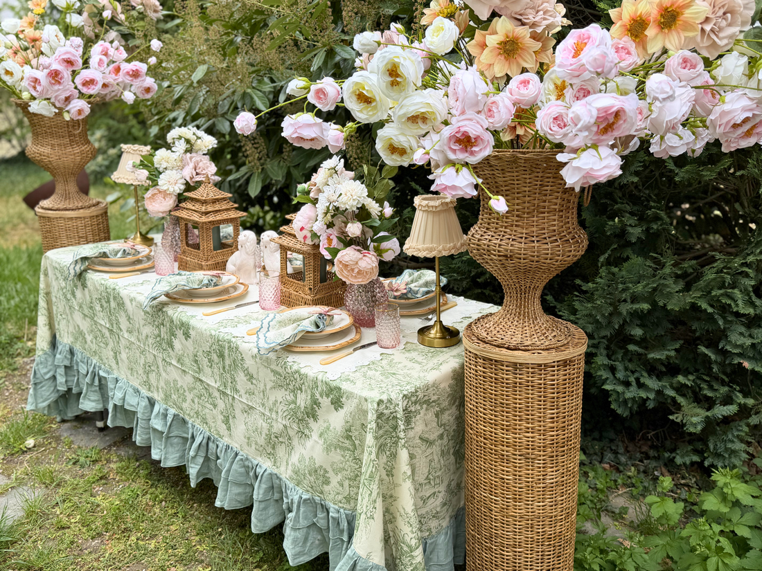 Gedeckter Tisch mit grüner Toile-de-Jouy-Tischdecke und rosa Rosen-Arrangements.