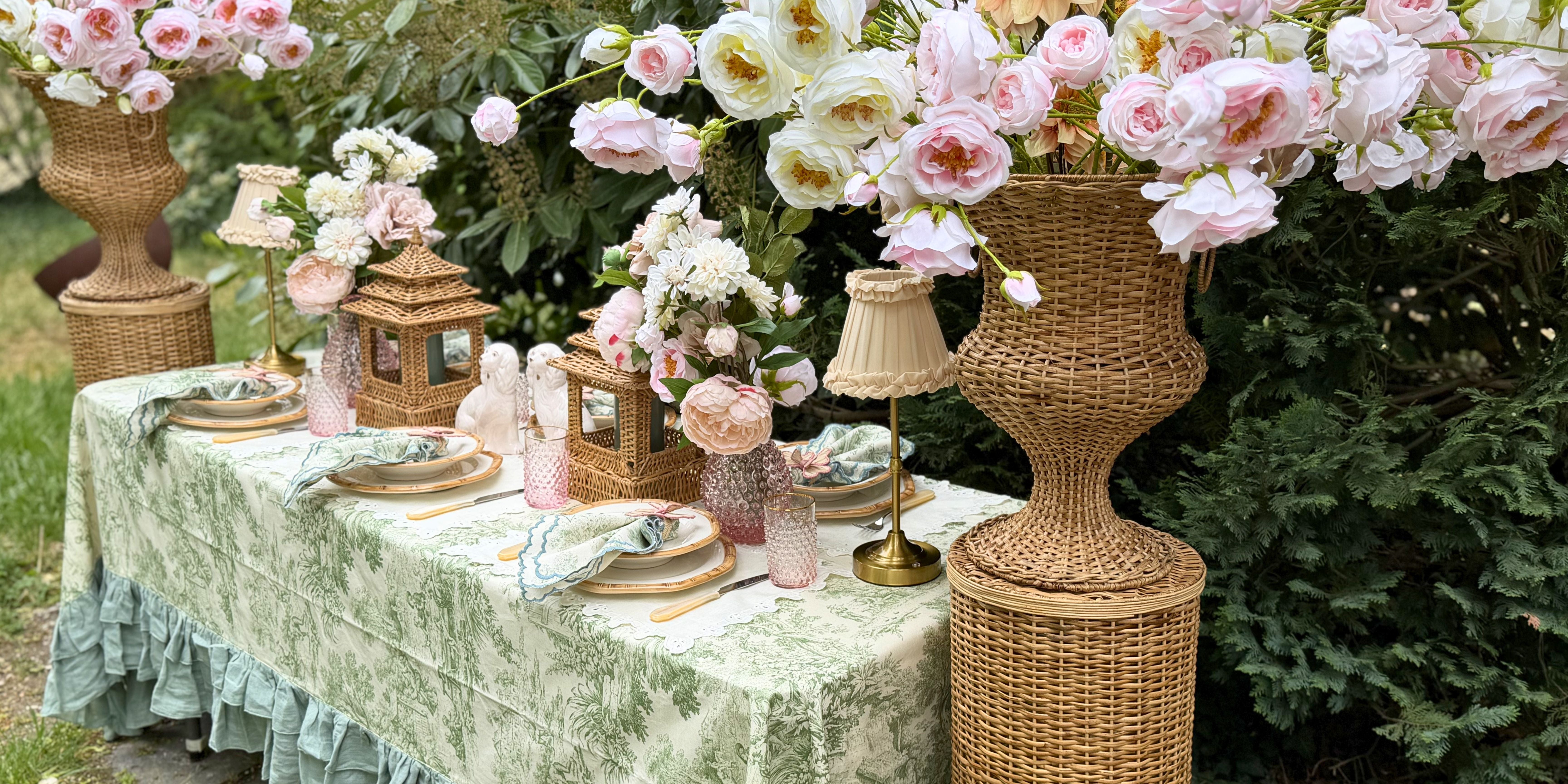 Romantisch gedeckter Tisch mit weißer Tischdecke, Rattan-Centerpiece, Bambus-Details und französischen Rosen.